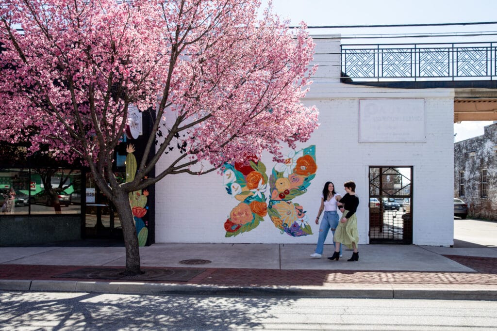 Girls walking under pink cherry blossoms on fifth street, butterfly mural on exterior of building behind them