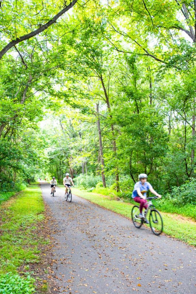 People biking on Percival's Island Blackwater Creek Trail surrounded by green trees