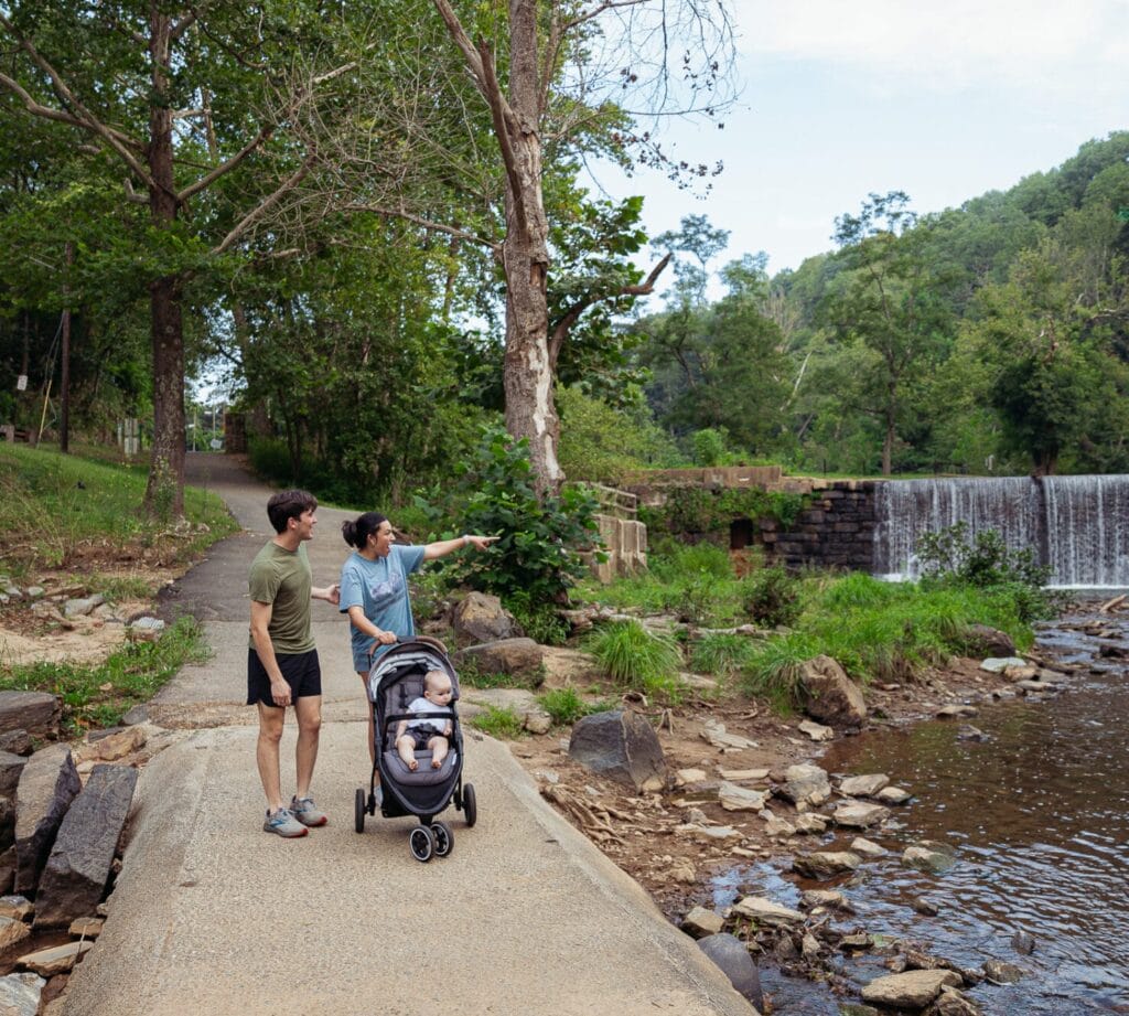 A family with a baby in stroller walking down trail at Hollins Mill surrounded by waterfall