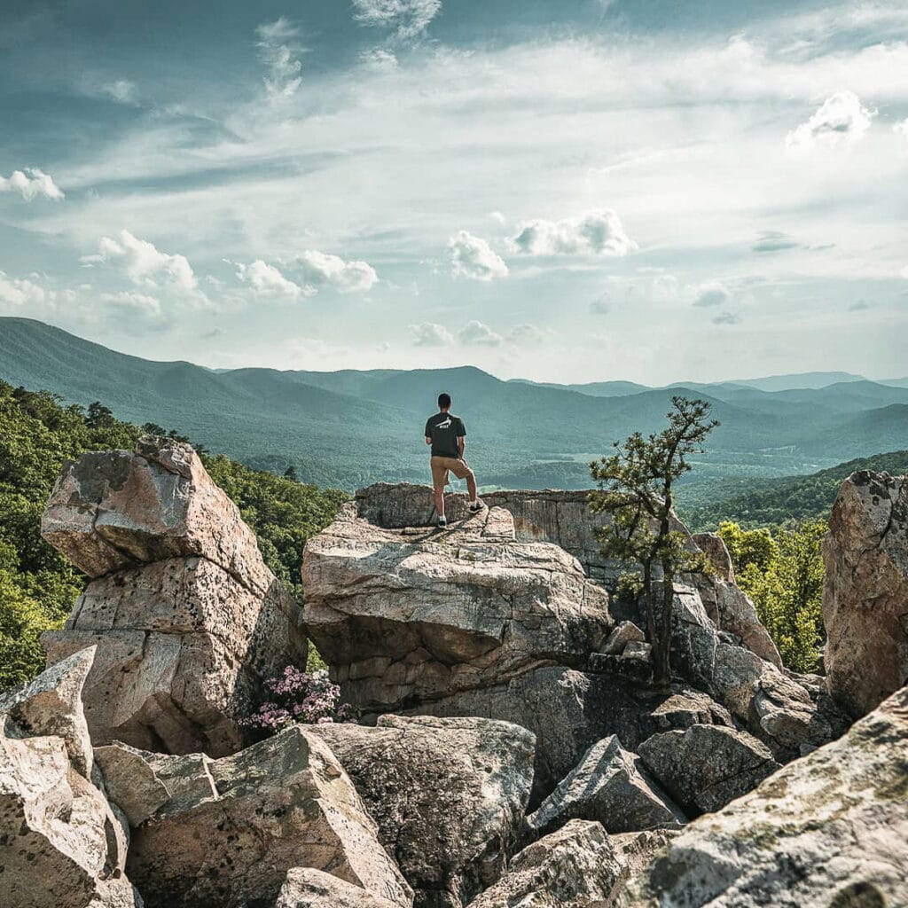 A guy standing on big rocks overlooking the blue ridge mountains